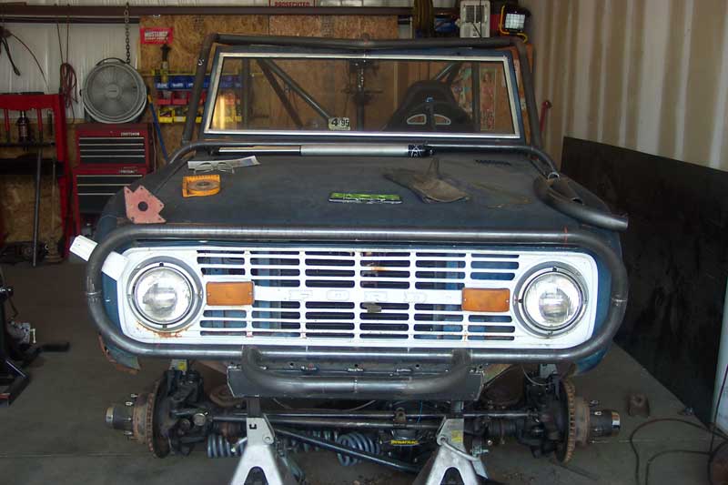 Front view of a 1974 Ford Bronco undergoing modifications with a roll cage and custom bumper