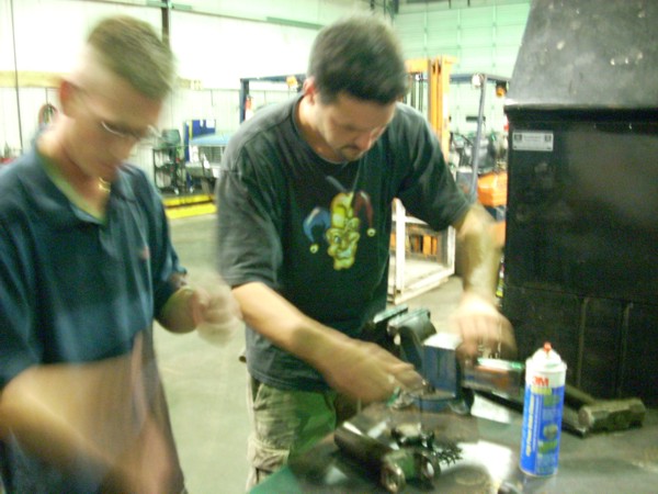 two guys working on a car part at a workbench