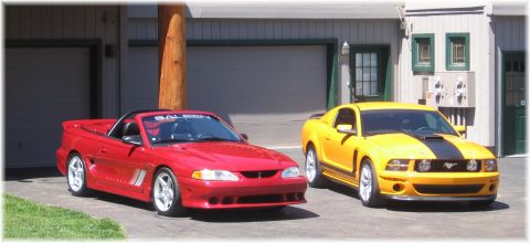 2007 Saleen S-302 - Two Ford Mustangs, a red convertible and a yellow coupe, are parked outside garages, with the red car displaying a Saleen banner.