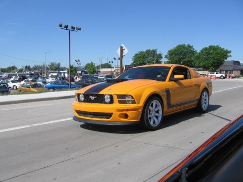 2007 Saleen S-302 - Orange 2007 Saleen S-302 Mustang with black stripe on hood, driving on a road.