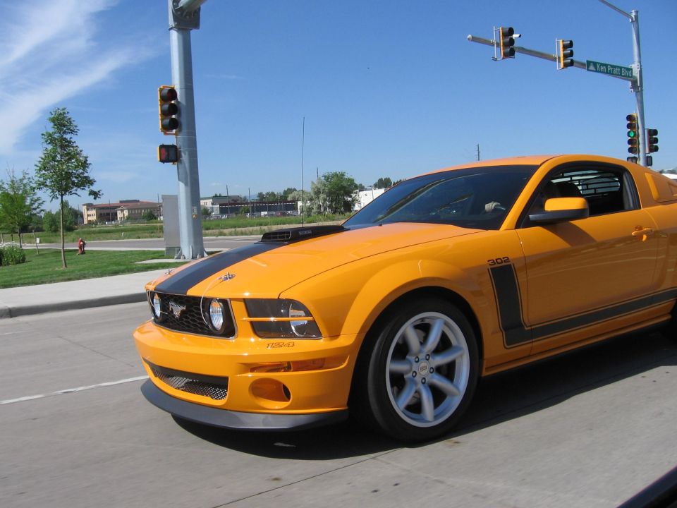 Yellow Ford Mustang with black stripes, driving on a sunny day