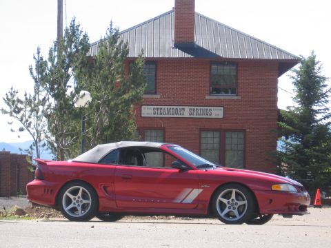 2007 Saleen S-302 - A red convertible Mustang is parked in front of a brick building with a sign that reads 'Steamboat Springs'.