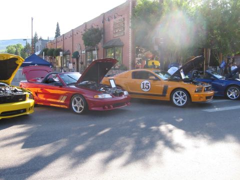2007 Saleen S-302 - Several Ford Mustangs are displayed with their hoods open on a sunny street in front of buildings.