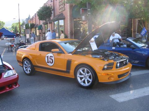 2007 Saleen S-302 - An orange Ford Mustang with racing decals and an open hood is parked on a street next to other vehicles.