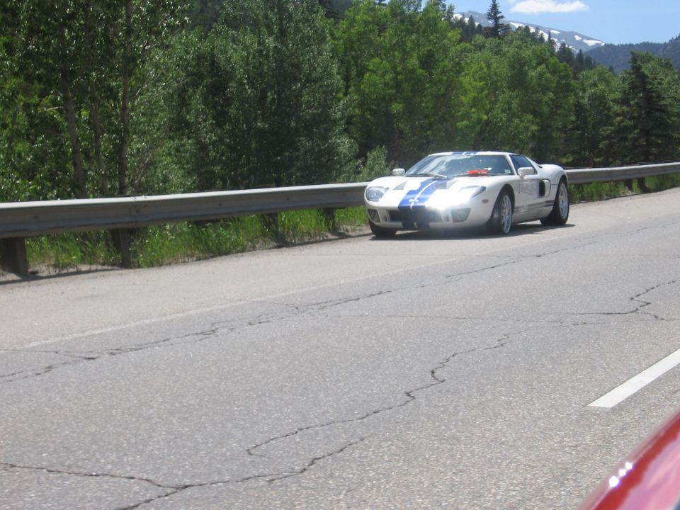 White 2005 Ford GT with blue stripes on a highway, front quarter view