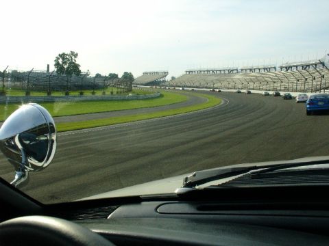 1993 Ford Mustang - A view from the driver's seat of a race track with multiple cars on the course and empty grandstands.