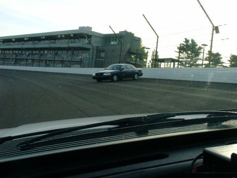 1993 Ford Mustang - A dark sedan, likely a police vehicle, drives on a race track with a grandstand in the background.