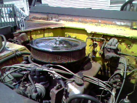 1974 Ford Bronco - The engine bay of a yellow 1974 Ford Bronco shows its V8 engine with a prominent chrome air filter housing.