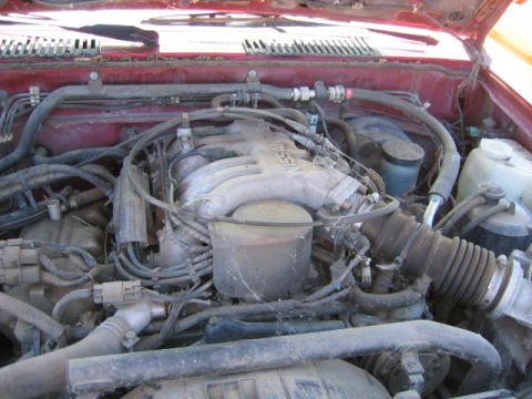 1973 Ford F-100 - The engine bay of a red vehicle, showing a Nissan engine with visible hoses and wiring.