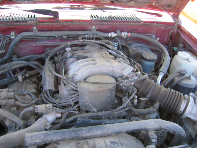 Red engine bay with Nissan branding on the intake manifold. Dusty and cluttered with hoses and wires
