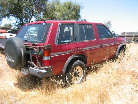 1973 Ford F-100 - Red SUV with spare tire on rear carrier, parked in tall dry grass.