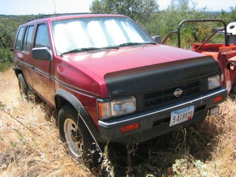 1973 Ford F-100 - This red Nissan Pathfinder is parked in a grassy area, with a sunshade visible through the windshield.