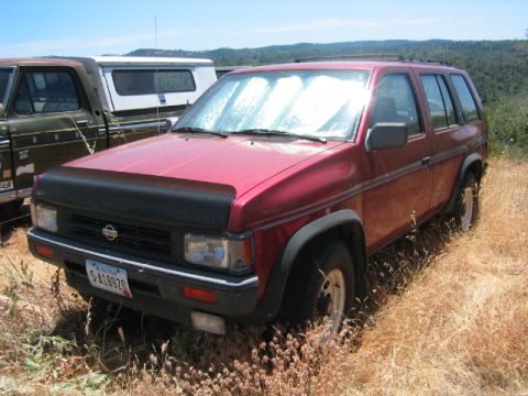 1973 Ford F-100 - A red Nissan Pathfinder SUV is parked in a field of dry grass next to a pickup truck.