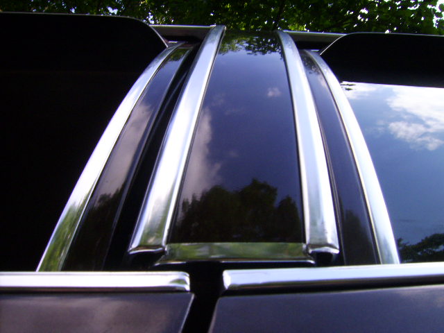 Close-up of black car's chrome window pillars reflecting sky and trees