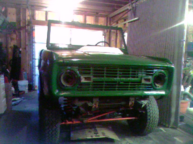 Green 1974 Ford Bronco front end, missing headlights, in a garage