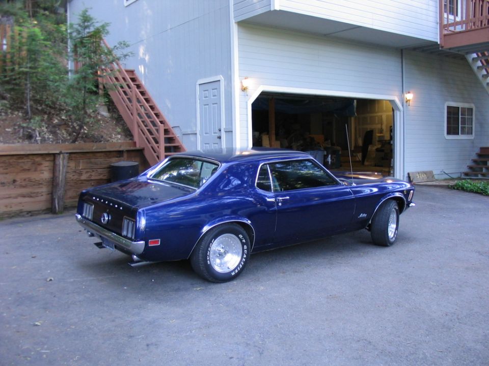 Blue 1970 Ford Mustang coupe parked in driveway next to a house