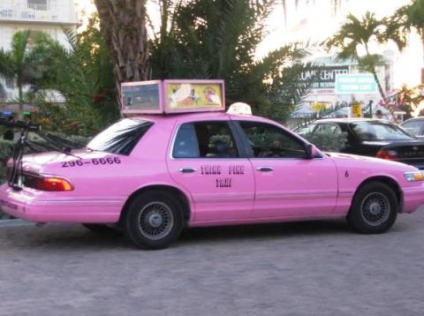 2001 Ford Crown Victoria - A pink 2001 Ford Crown Victoria taxi is parked on a street with a bicycle rack attached to its rear.