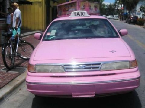 2001 Ford Crown Victoria - A pink taxi with a "TAXI" sign on its roof is parked on the street.