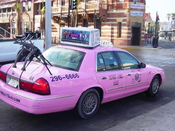 Pink taxi cab with a bike rack on the trunk, parked on a street