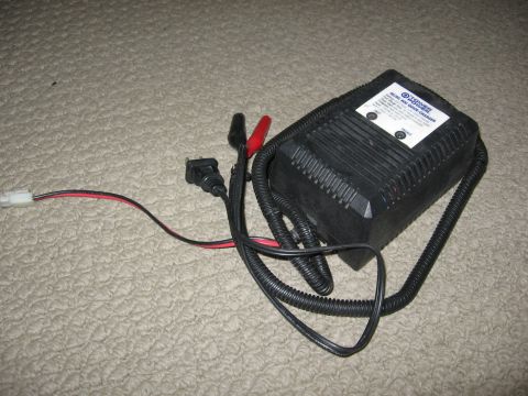 1974 Ford F-100 - A black battery charger with attached cables and clips rests on a textured surface.