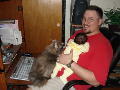 2000 Ford Crown Victoria - Man holding a baby while a cat looks up, with a computer desk in the background.