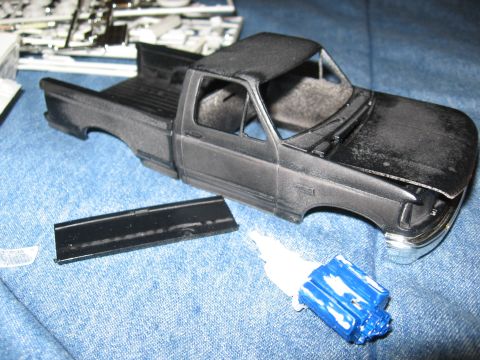 1974 Ford F-100 - Plastic model truck body and parts laid out on a blue fabric surface, with a tube of glue nearby.