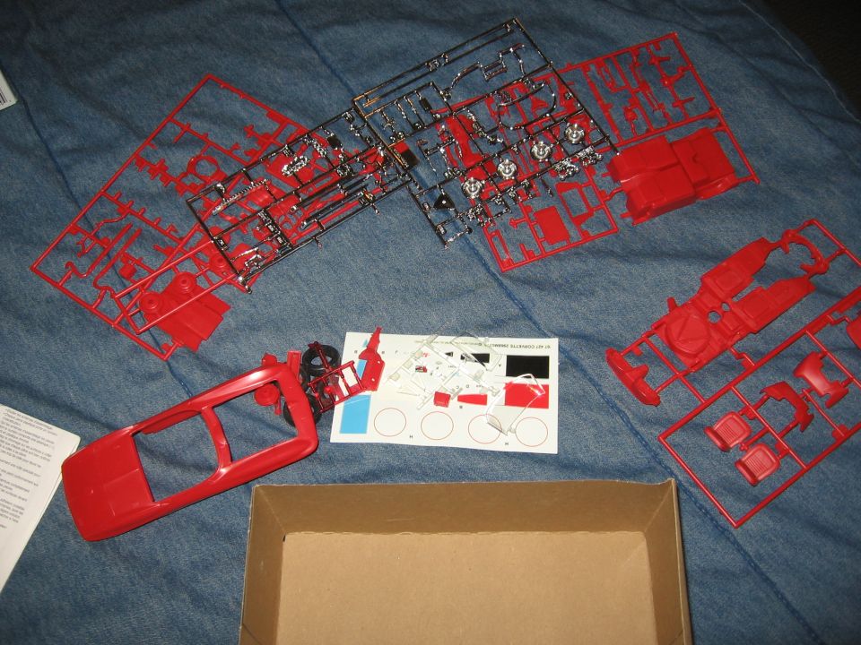 Red plastic model car parts on a blue surface, with a decal sheet and an open box