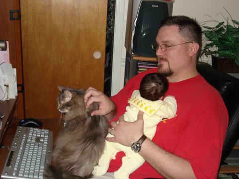 2000 Ford Crown Victoria - A man is seated indoors, holding a baby and a cat, with a computer setup in the background.