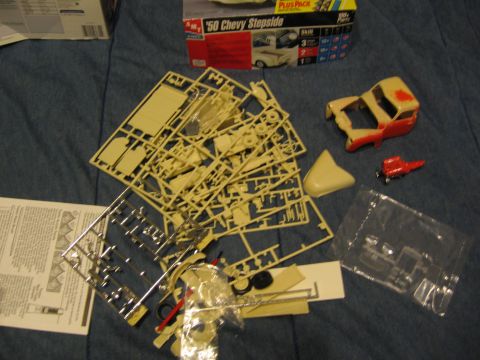 1974 Ford F-100 - Unassembled plastic model kit parts and instructions are laid out on a blue surface, with a box for a '50 Chevy Stepside visible.