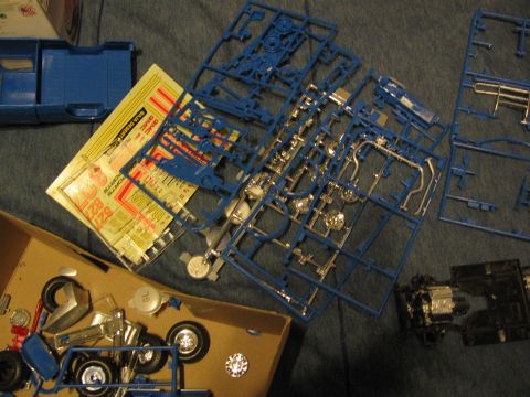 1974 Ford F-100 - Plastic model kit parts, including a blue truck body and chrome engine components, are laid out with decals.