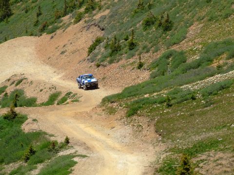 1987 Ford Bronco - A pickup truck navigates a steep, unpaved mountain road under a clear sky.