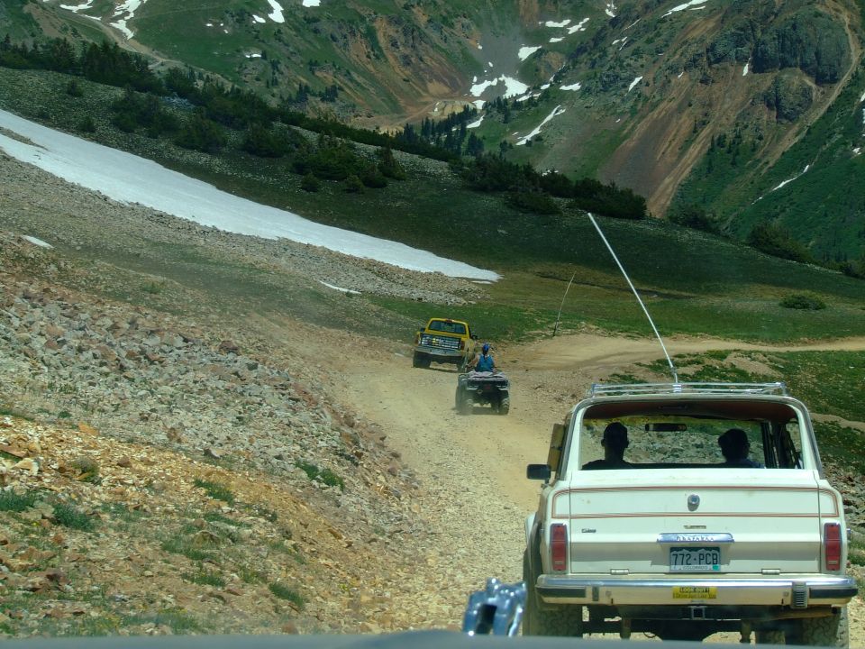 Cream-colored SUV with roof rack driving on a dirt road, license plate 772-PCB