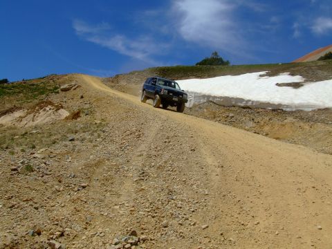 1987 Ford Bronco - SUV navigates a challenging mountain trail under a clear blue sky.