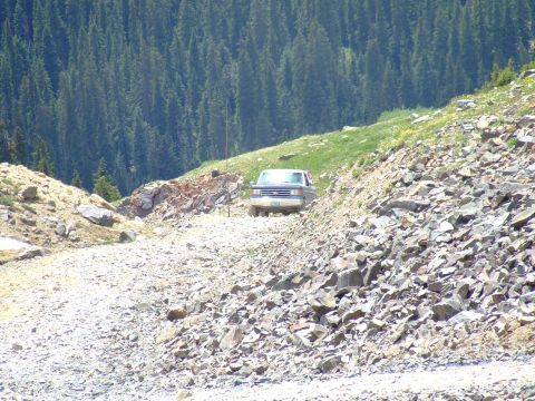 1987 Ford Bronco - 1987 Ford Bronco navigates a challenging, rocky mountain pass with dense forest scenery.