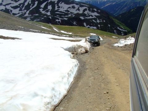 1987 Ford Bronco - A Jeep navigates a snowy mountain road, with another vehicle's side visible in the foreground.