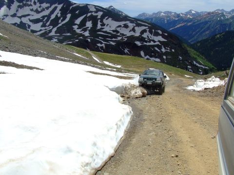 1987 Ford Bronco - A dark green SUV navigates a snowy mountain pass.