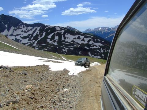 1987 Ford Bronco - Two vehicles navigate a challenging mountain pass with snow patches and terrain.