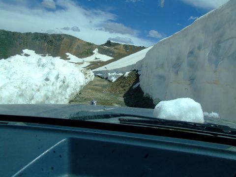 1987 Ford Bronco - Navigating a treacherous mountain road, flanked by towering snowbanks under a partly cloudy sky.