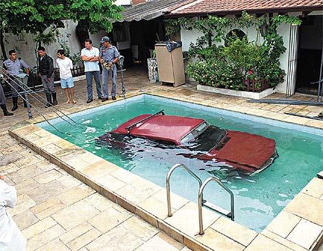1991 Ford Taurus - A red car is partially submerged in a swimming pool while onlookers observe the scene.