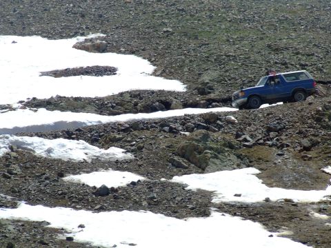 1987 Ford Bronco - A blue 1987 Ford Bronco navigates a challenging, snow-dusted mountain terrain.
