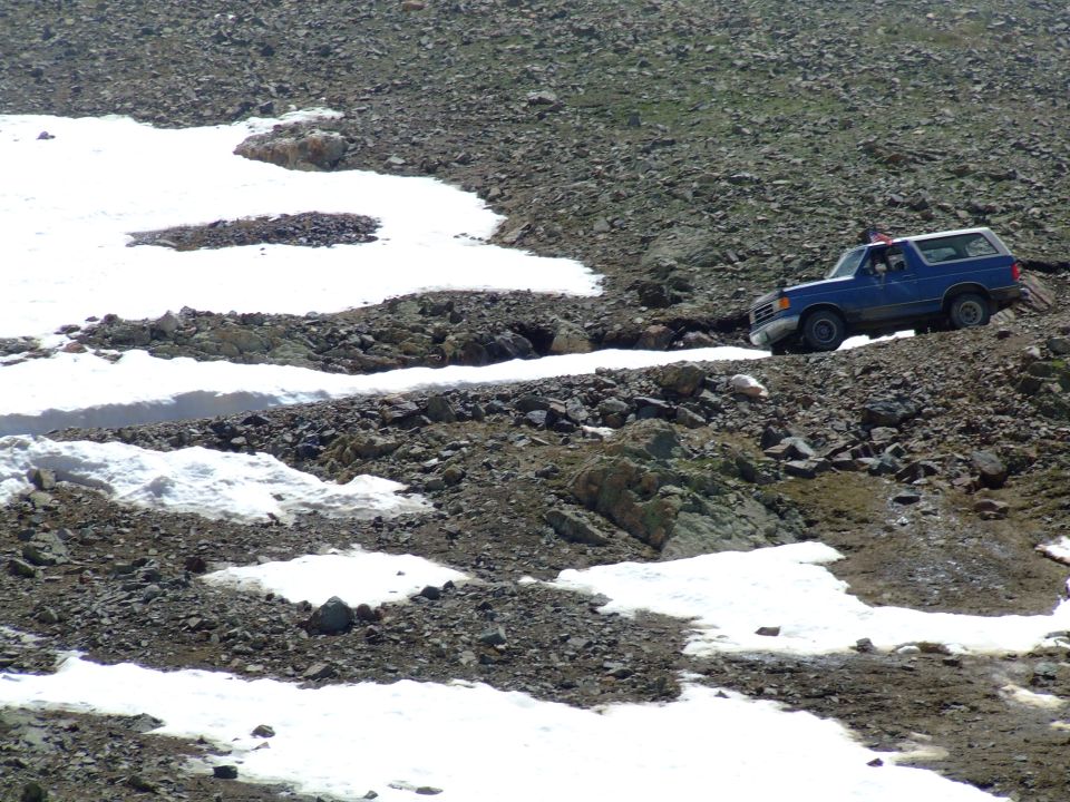 Blue 1987 Ford Bronco driving on a rocky, snowy mountain path