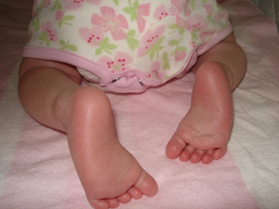 Baby's feet and legs on a pink blanket, wearing a floral onesie