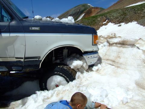 1987 Ford Bronco - This Ford Bronco is partially buried in snow, with a person attempting to free it from the drift.