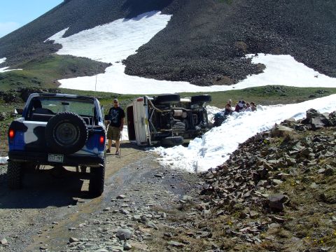 1987 Ford Bronco - An off-road adventure takes a turn as one vehicle ends up on its side on a snowy mountain path, while another waits.
