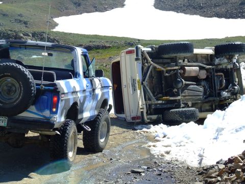 1987 Ford Bronco - A Ford Bronco is parked next to a flipped-over van on a dirt road with snow patches.