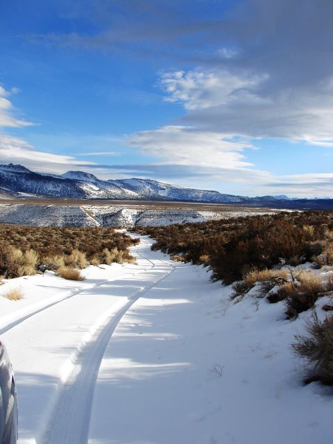 1996 Ford Bronco - A vehicle drives on a snowy road through a barren landscape towards distant mountains.