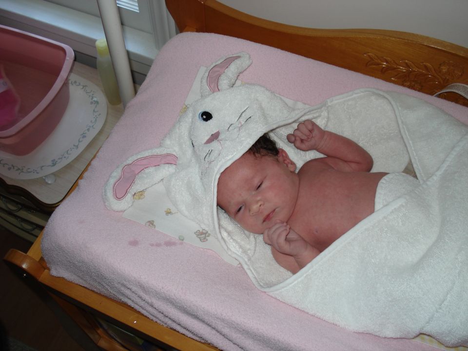Baby wrapped in a white bunny hooded towel on a pink blanket