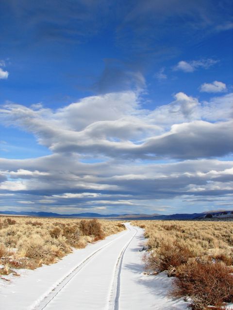 1996 Ford Bronco - A road covered in snow winds through a dry, arid landscape with mountains in the distance.