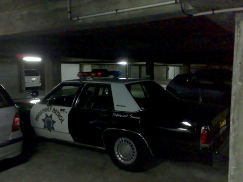 1991 Ford Crown Victoria - A black and white police car with emergency lights on top is parked in a garage.
