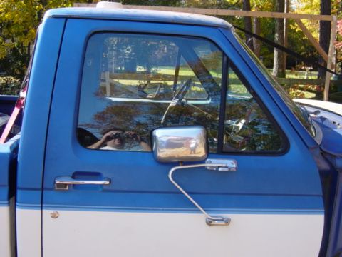 1985 Ford F-250 - The side profile of a two-tone blue and white Ford F-250 pickup truck is visible, with reflections in the window.